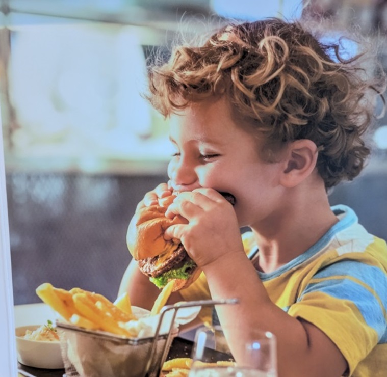 Junge beißt genüßlich in einem Burger im Restaurant BestBurger@sea auf der AIDAmar